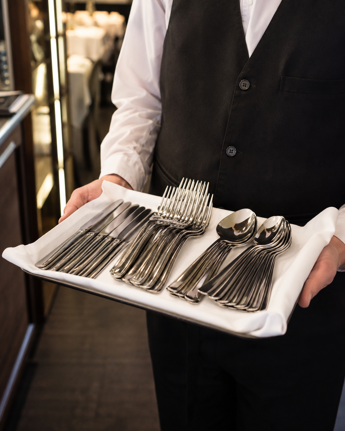 Servicekraft transportiert sortiertes Restaurantbesteck sicher auf einem mit Stoff ausgelegten Tablett.