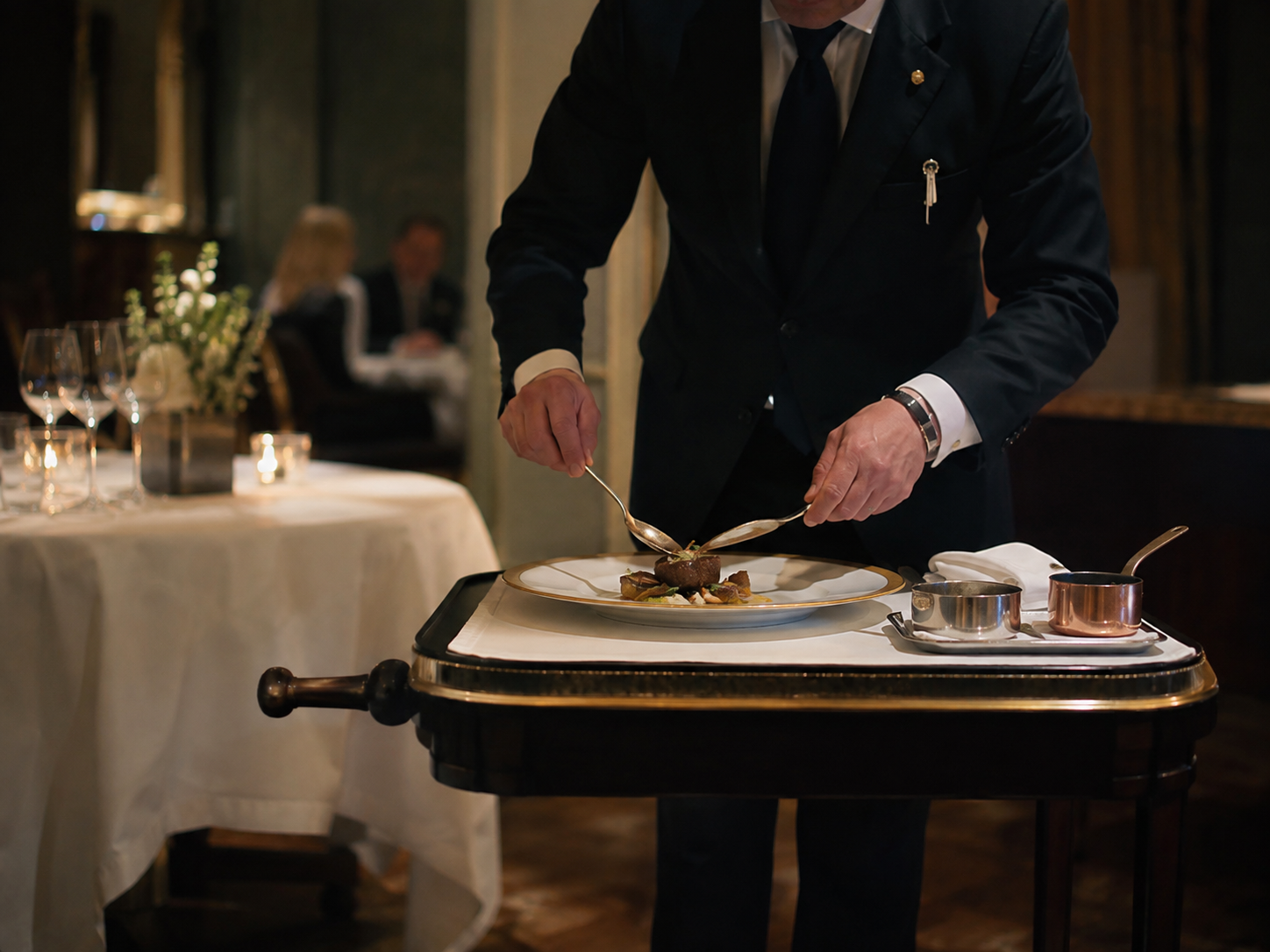 Servicekraft richtet ein Gericht am Gueridon mit Besteck und Saucieren an.