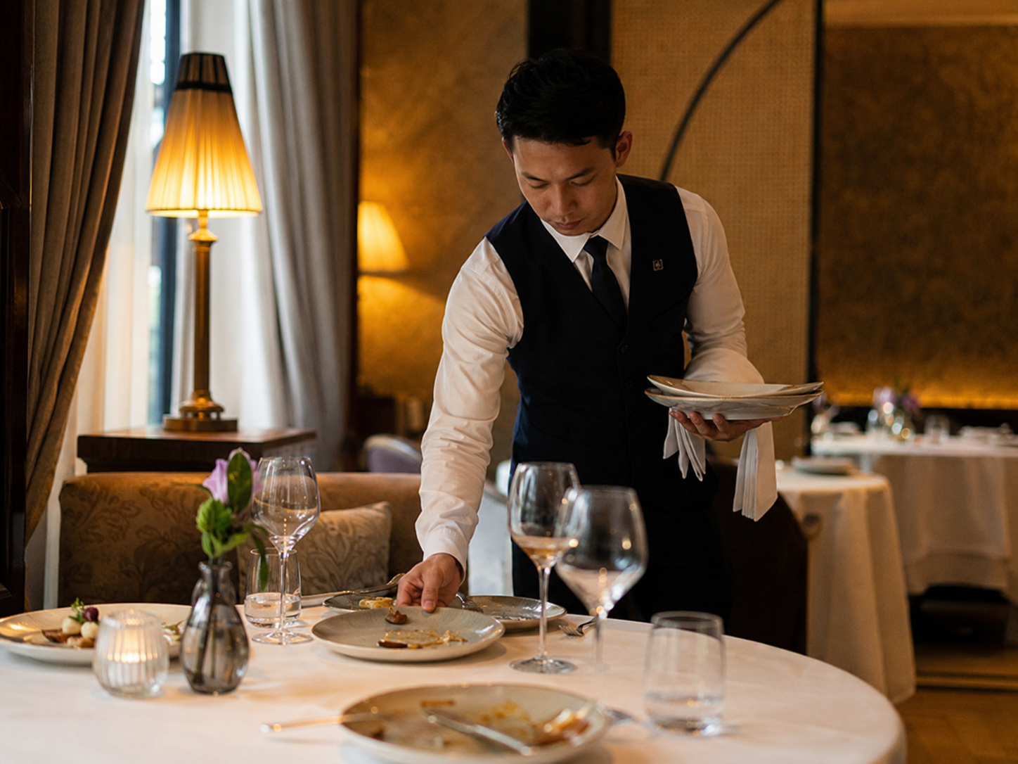 Servicemitarbeiter räumt benutzte Teller an einem gedeckten Restauranttisch ab